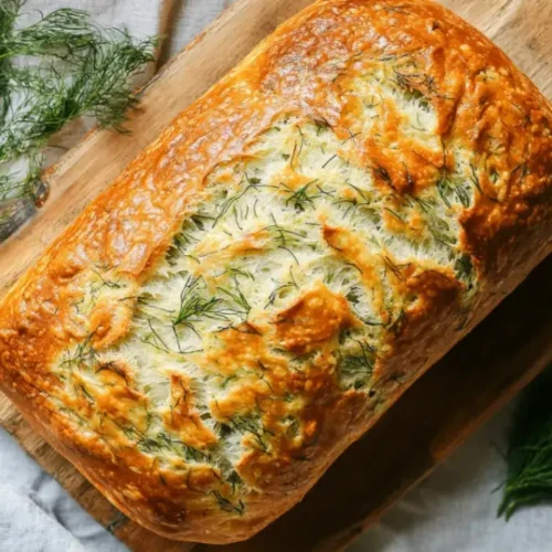 Top-down view of homemade dill bread on a wooden cutting board with butter and fresh dill.