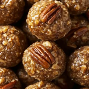 Top-down, high-resolution photo of a rustic wooden platter filled with glossy, bite-sized pecan pie balls coated in chopped pecans, arranged neatly with a few whole pecans scattered around. The balls have a rich, golden-brown color and a creamy texture visible beneath the nut coating. Soft natural lighting highlights the glossy sheen and crunchy texture, evoking a homemade, festive feel.